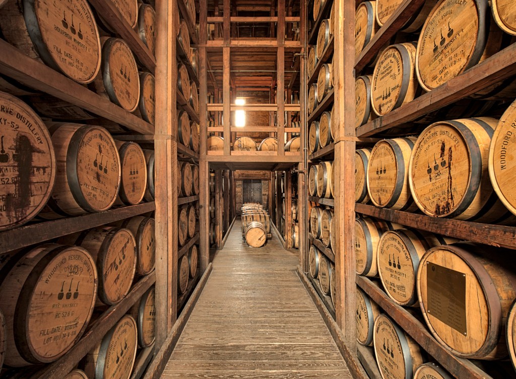 Interior view of a whisky barrel storage facility, featuring wooden barrels stacked on shelves and a wooden walkway between them.